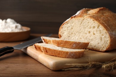 Photo of Cut tasty sodawater bread and wheat spikes on wooden table