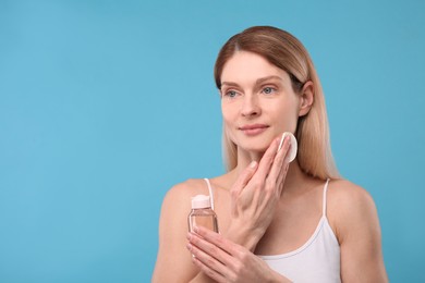 Photo of Beautiful woman removing makeup with cotton pad on light blue background, space for text