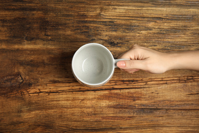 Photo of Woman with empty cup at wooden table, top view