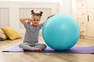Little cute girl with fitness ball at home. Doing exercises