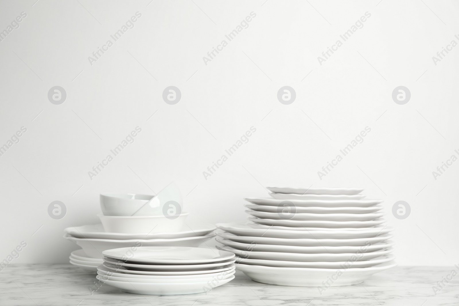 Photo of Set of clean plates and bowls on marble table against white background. Space for text