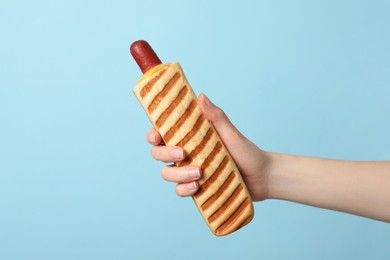 Photo of Woman holding delicious french hot dog on light blue background, closeup