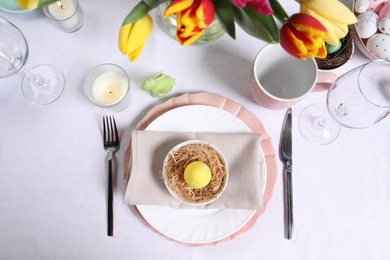 Photo of Festive table setting with painted egg in decorative nest, flat lay. Easter celebration