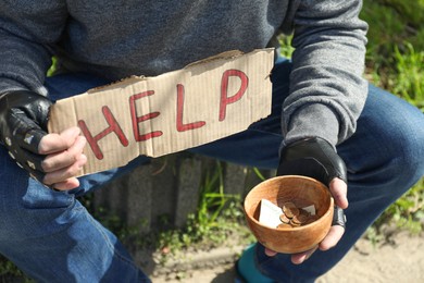 Poor homeless man holding help sign and bowl with donations outdoors, closeup