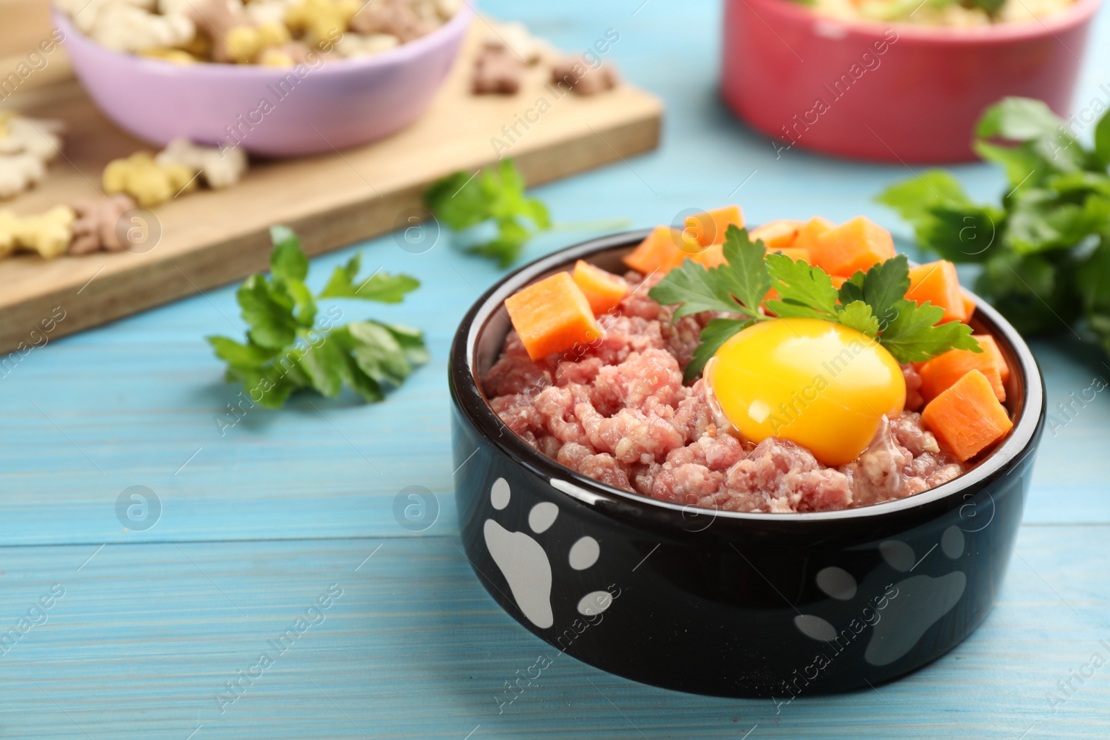 Photo of Natural pet food in feeding bowl on light blue wooden table, closeup. Space for text