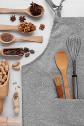 Flat lay composition with grey apron, ingredients and kitchen utensils on white table