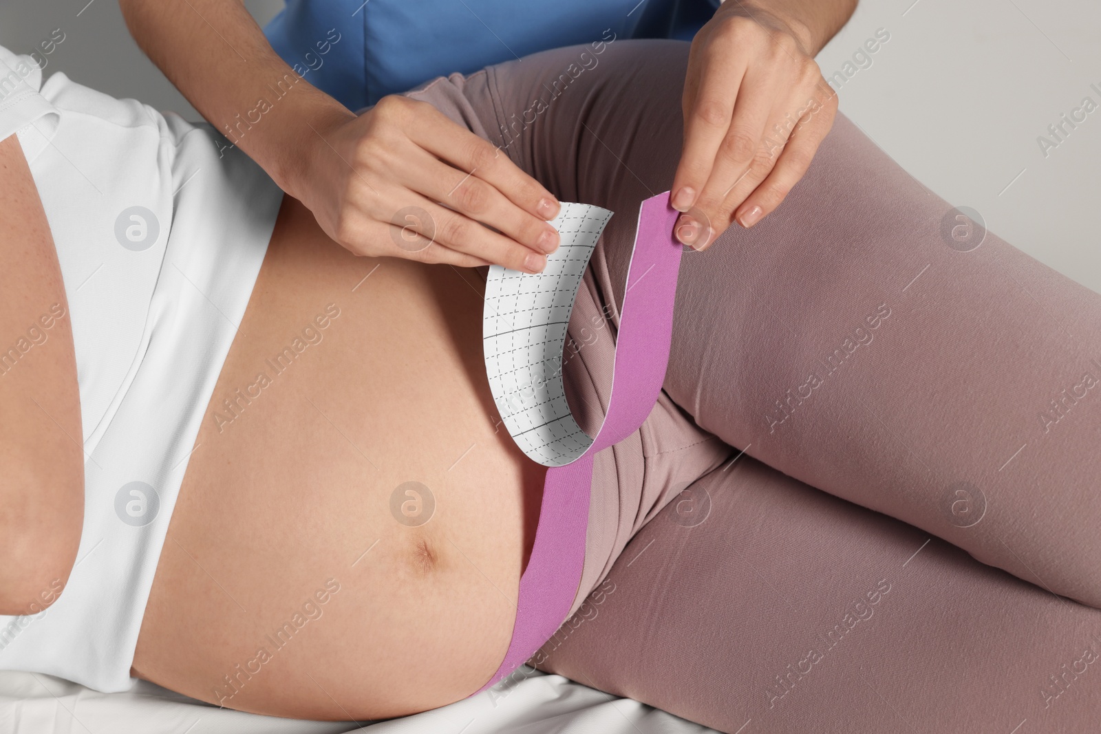 Photo of Pregnant woman visiting physiotherapist. Doctor applying kinesio tape on couch, closeup