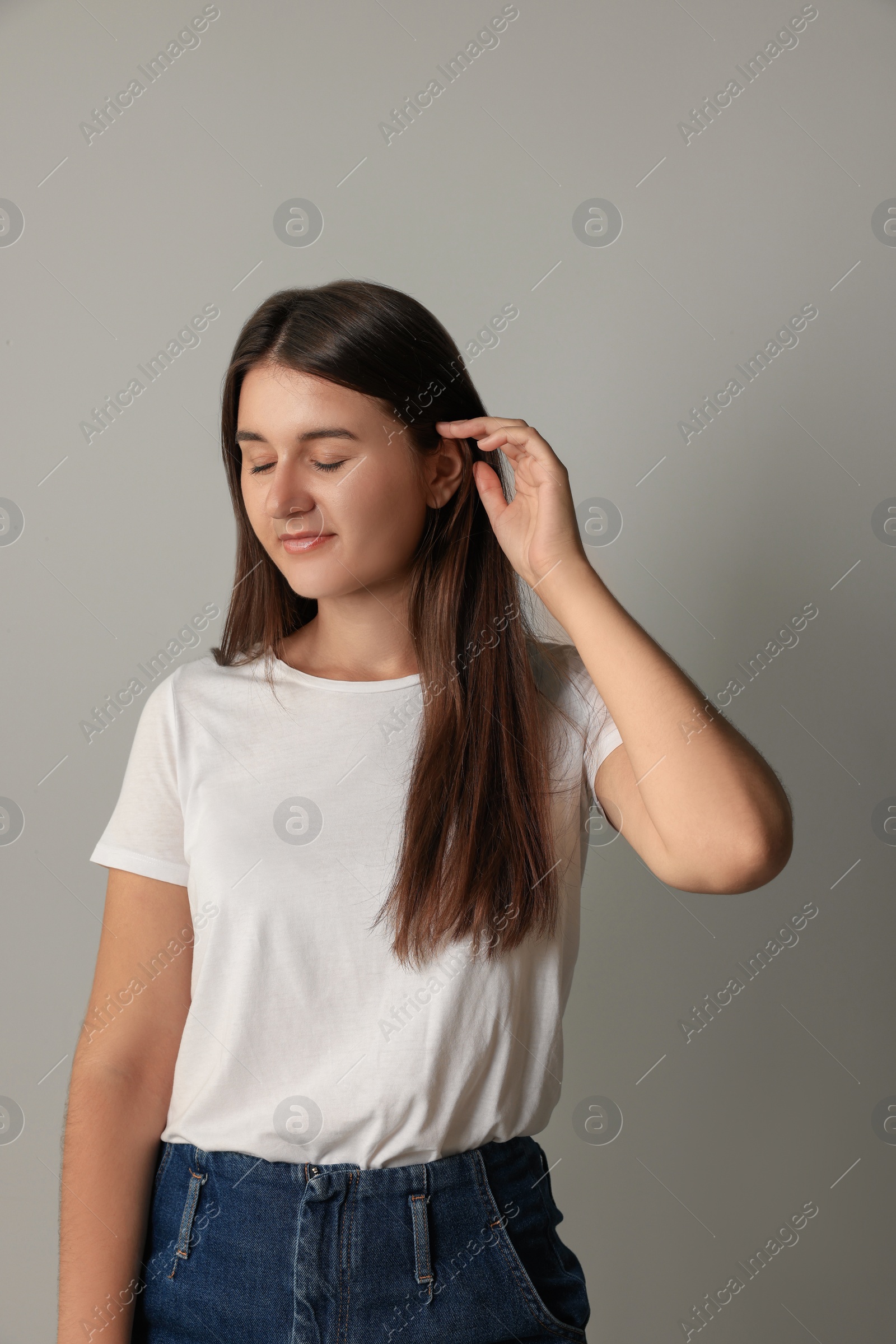 Photo of Beautiful young woman with closed eyes touching her hair on light grey background