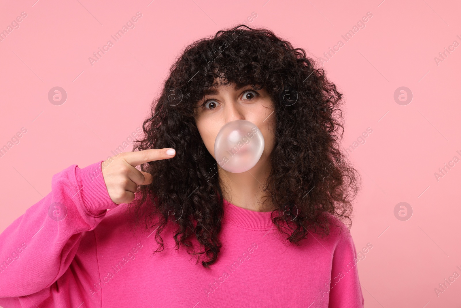 Photo of Beautiful young woman blowing bubble gum on pink background