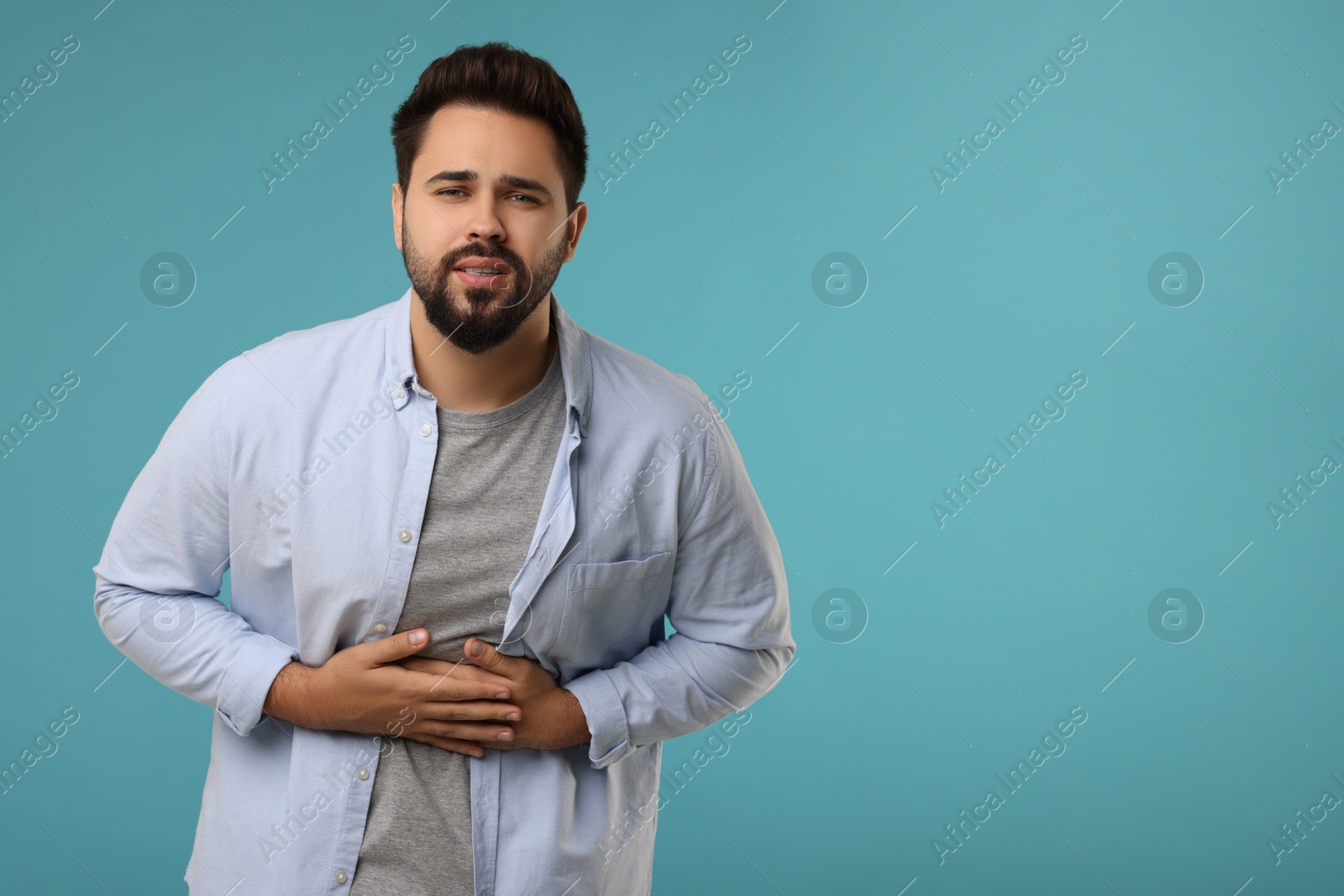 Photo of Young man suffering from stomach pain on light blue background. Space for text