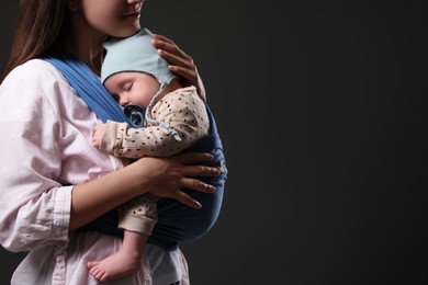 Photo of Mother holding her child in sling (baby carrier) on black background, closeup. Space for text