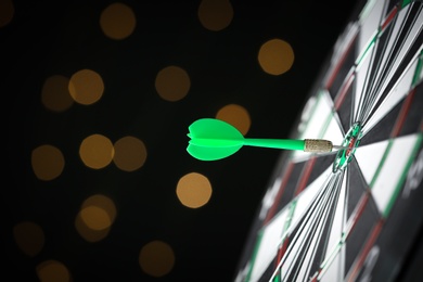 Photo of Green arrow hitting target on dart board against blurred lights. Space for text