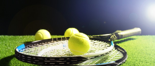 Tennis rackets and balls on green grass against dark background, space for text. Banner design
