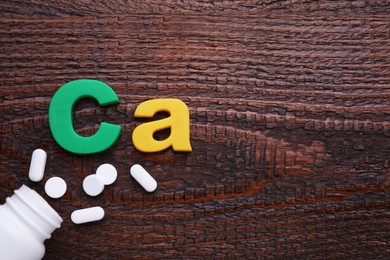 Photo of Paper symbol Ca (Calcium), medical bottle and pills on wooden table, top view. Space for text