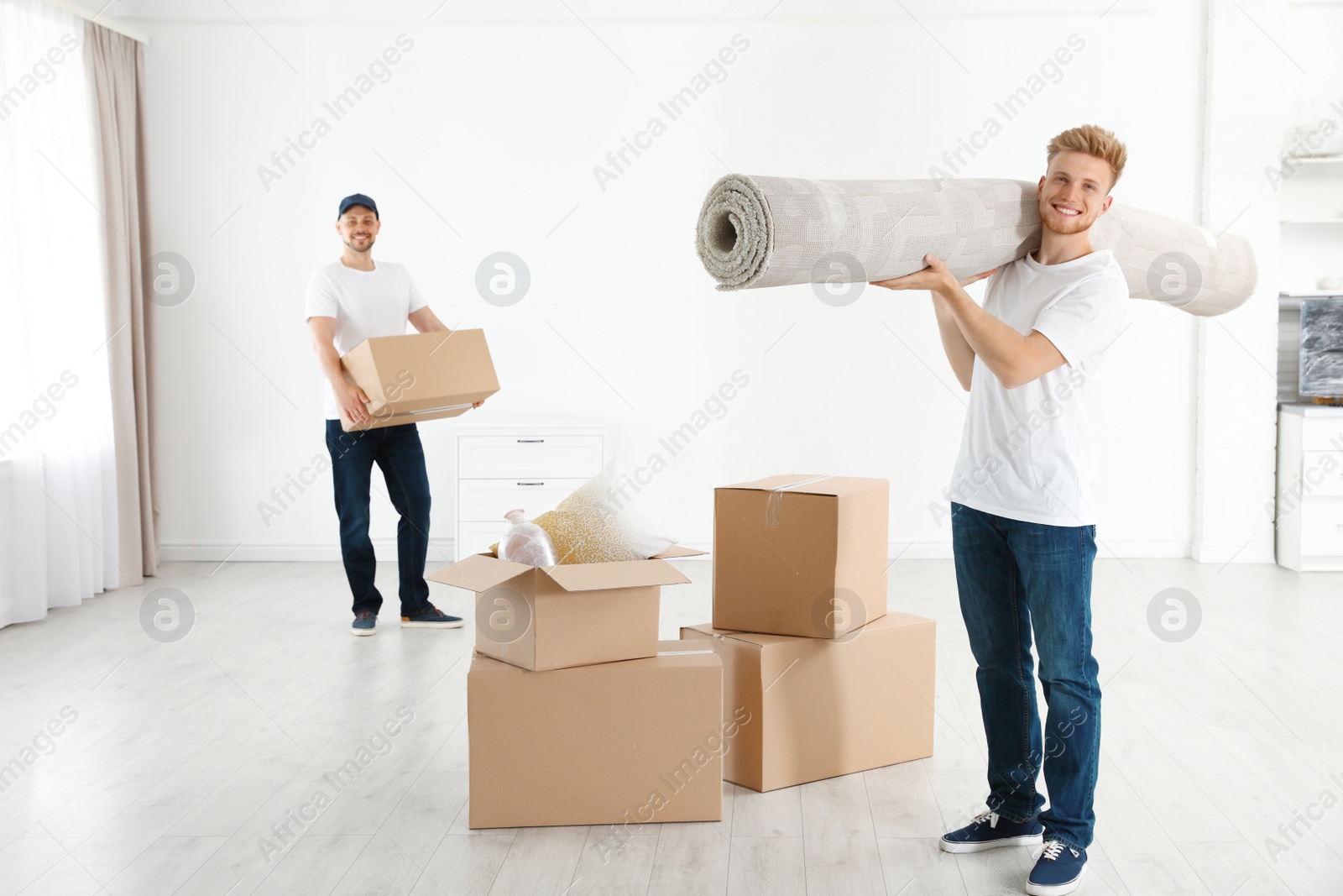 Photo of Moving service employees with cardboard boxes and carpet in room