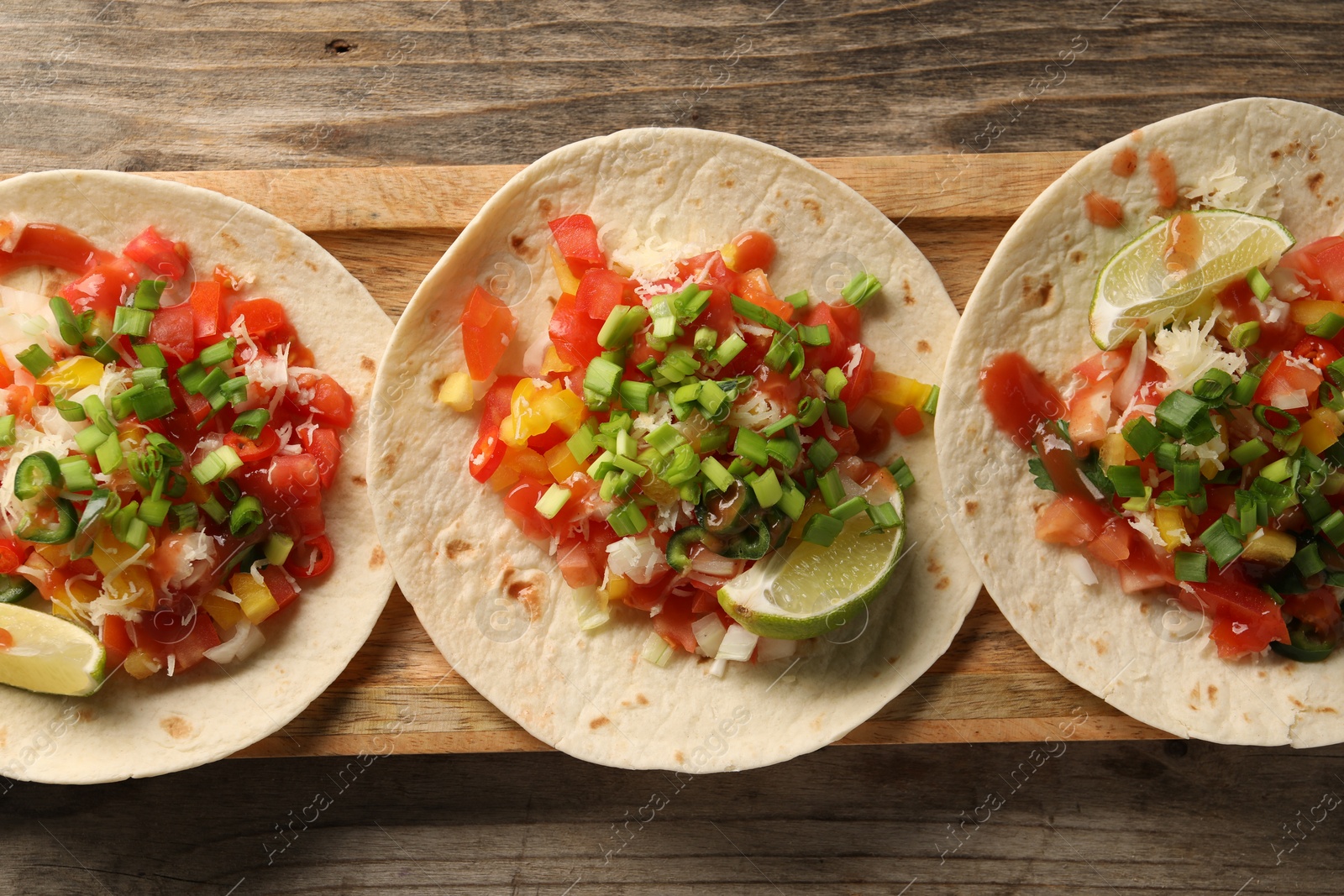 Photo of Delicious tacos with vegetables, green onion, lime and ketchup on wooden table, top view