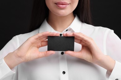 Woman holding blank business card on black background, closeup. Space for text