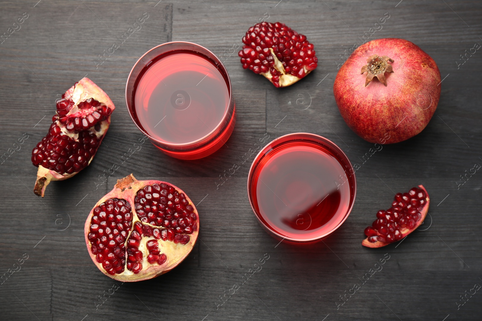 Photo of Tasty pomegranate juice in glasses and fresh fruits on black wooden table, flat lay