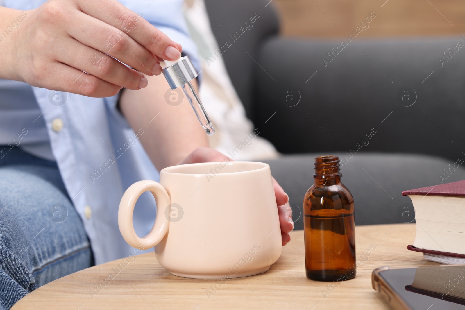 Photo of Woman dripping food supplement into cup at wooden table indoors, closeup