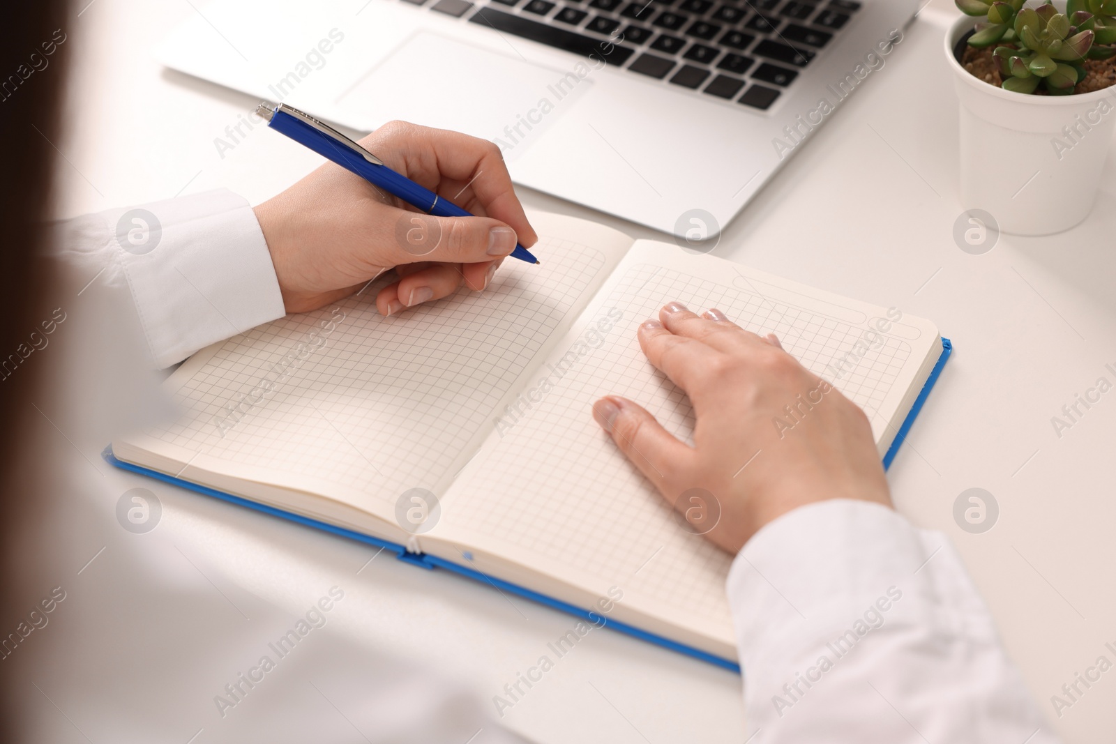 Photo of Young woman writing in notebook at white table, closeup