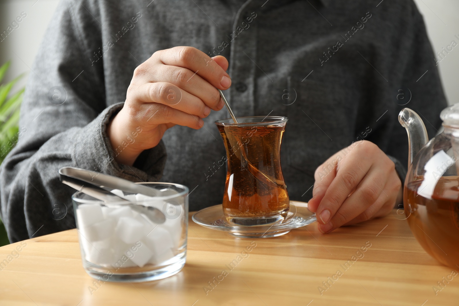 Photo of Woman stirring sugar in tea at wooden table, closeup