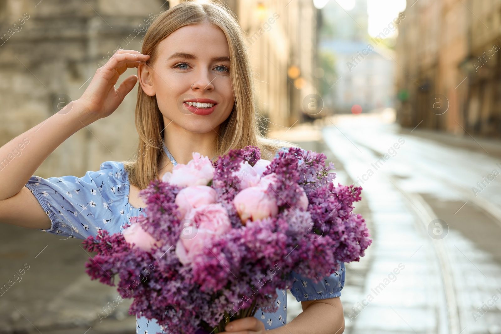 Photo of Beautiful woman with bouquet of spring flowers on city street, space for text