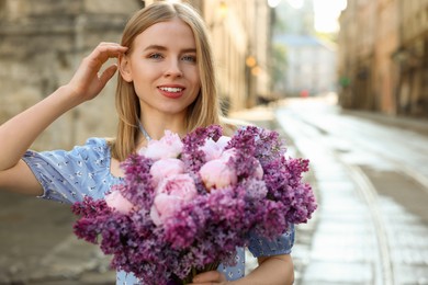 Photo of Beautiful woman with bouquet of spring flowers on city street, space for text