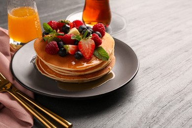 Delicious pancakes with fresh berries, honey and butter served on grey table, closeup. Space for text