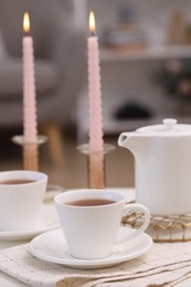 Cups of tea, teapot and burning candles on white table indoors