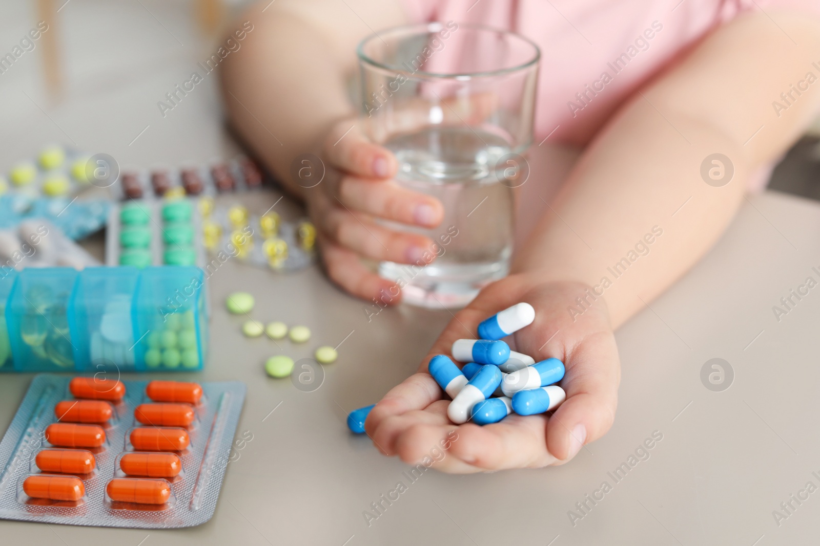 Photo of Little child with many different pills and water at table, closeup. Danger of medicament intoxication