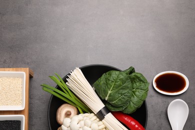 Photo of Cooking delicious ramen soup. Different ingredients in bowls and spoon on gray table, flat lay. Space for text