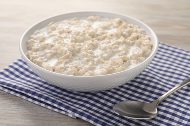 Photo of Tasty boiled oatmeal in bowl and spoon on wooden table, closeup