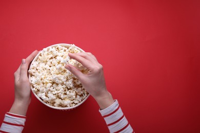 Woman taking delicious popcorn from paper bucket on red background, top view. Space for text