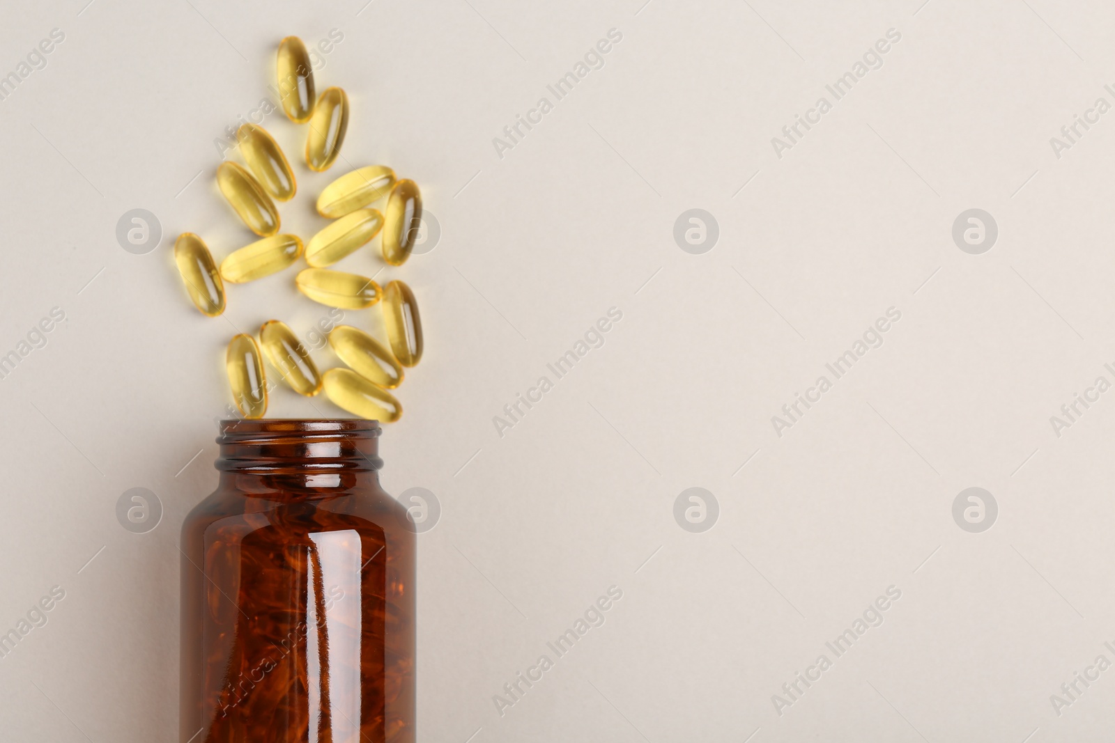 Photo of Bottle and vitamin capsules on light grey background, top view. Space for text