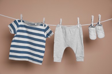 Photo of Cute small baby shoes and clothes hanging on washing line against brown background