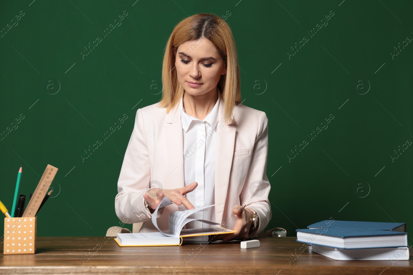 Photo of Portrait of beautiful teacher sitting at table near chalkboard