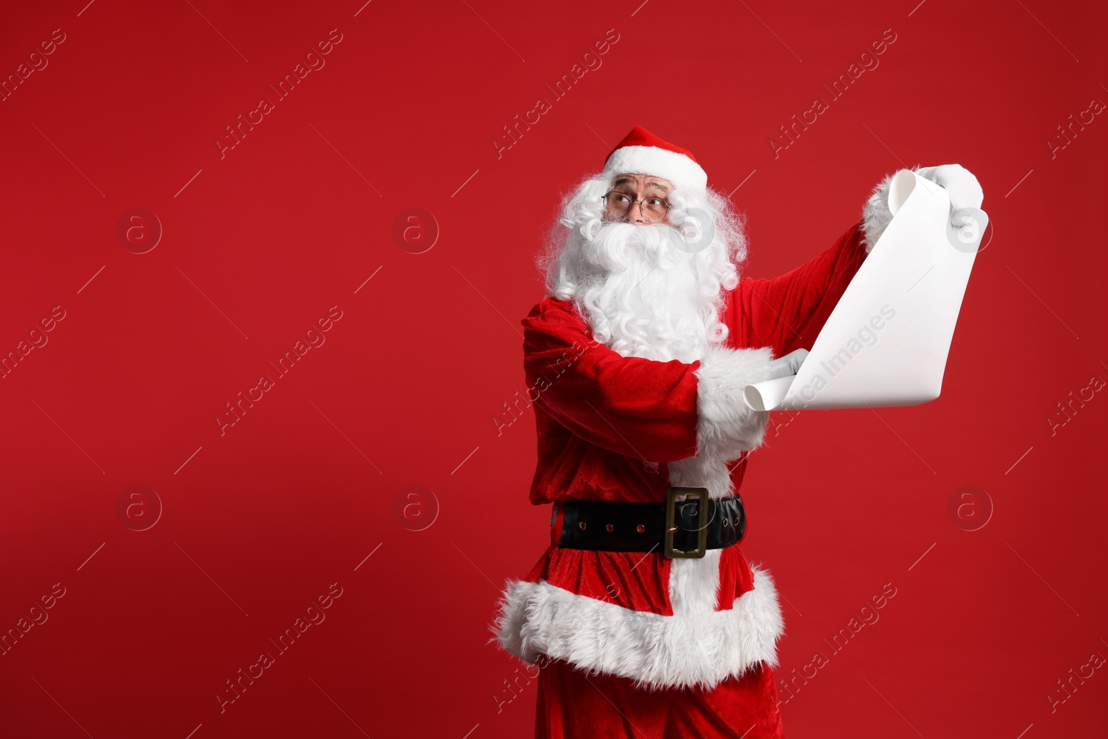 Photo of Merry Christmas. Santa Claus holding wishlist on red background, space for text
