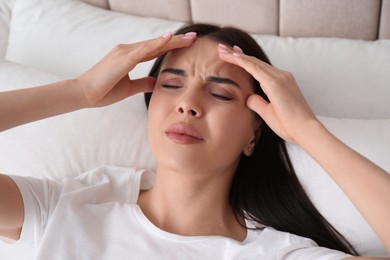 Photo of Young woman suffering from migraine in bed, above view