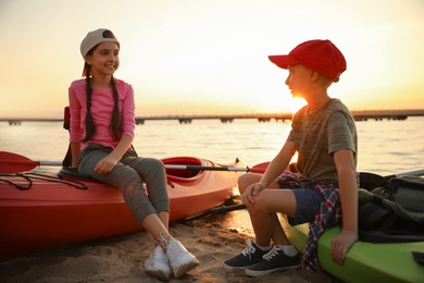 Photo of Happy children sitting on kayaks near river at sunset. Summer camp