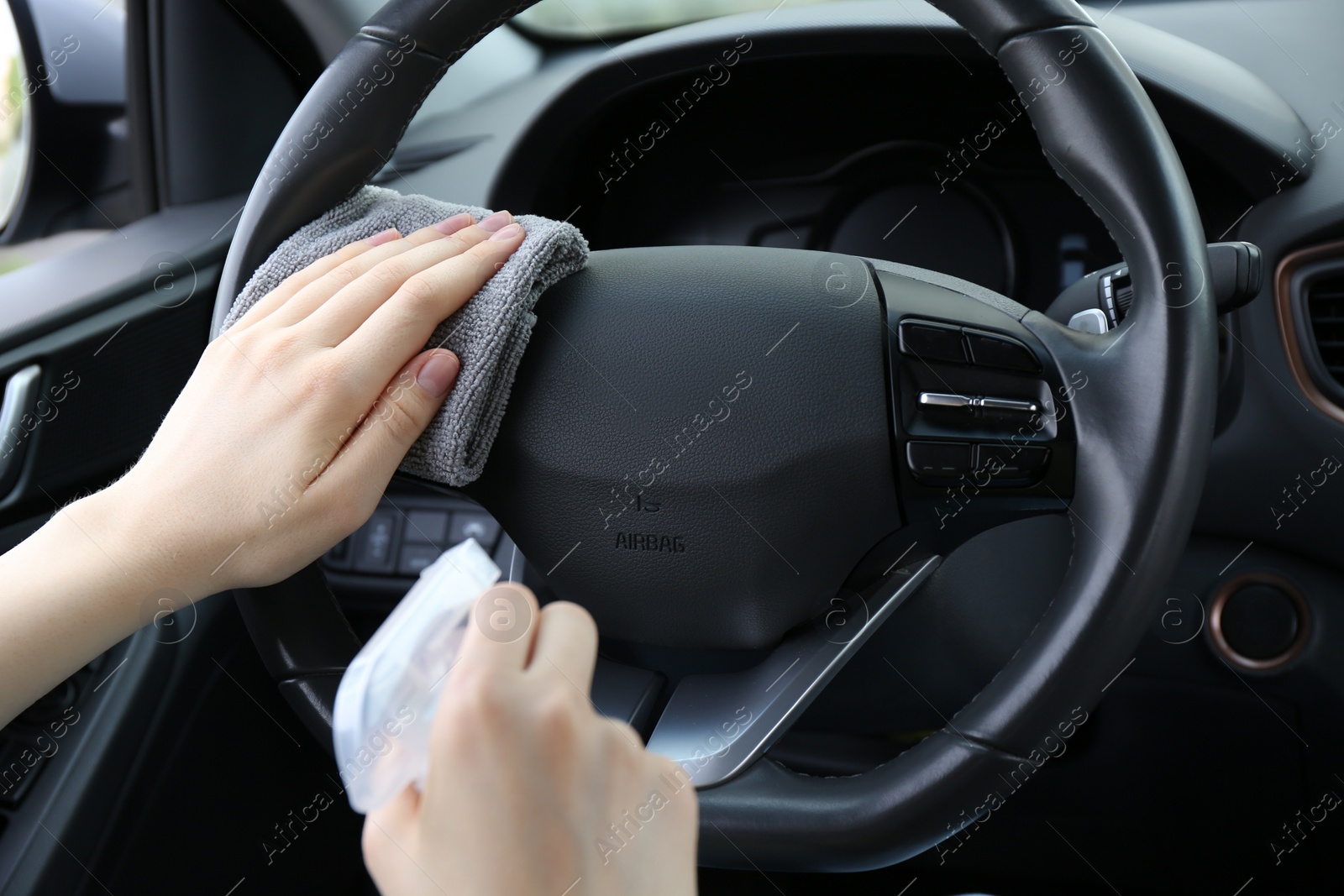 Photo of Woman cleaning steering wheel with rag in car, closeup