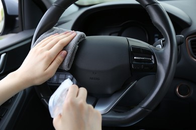 Photo of Woman cleaning steering wheel with rag in car, closeup