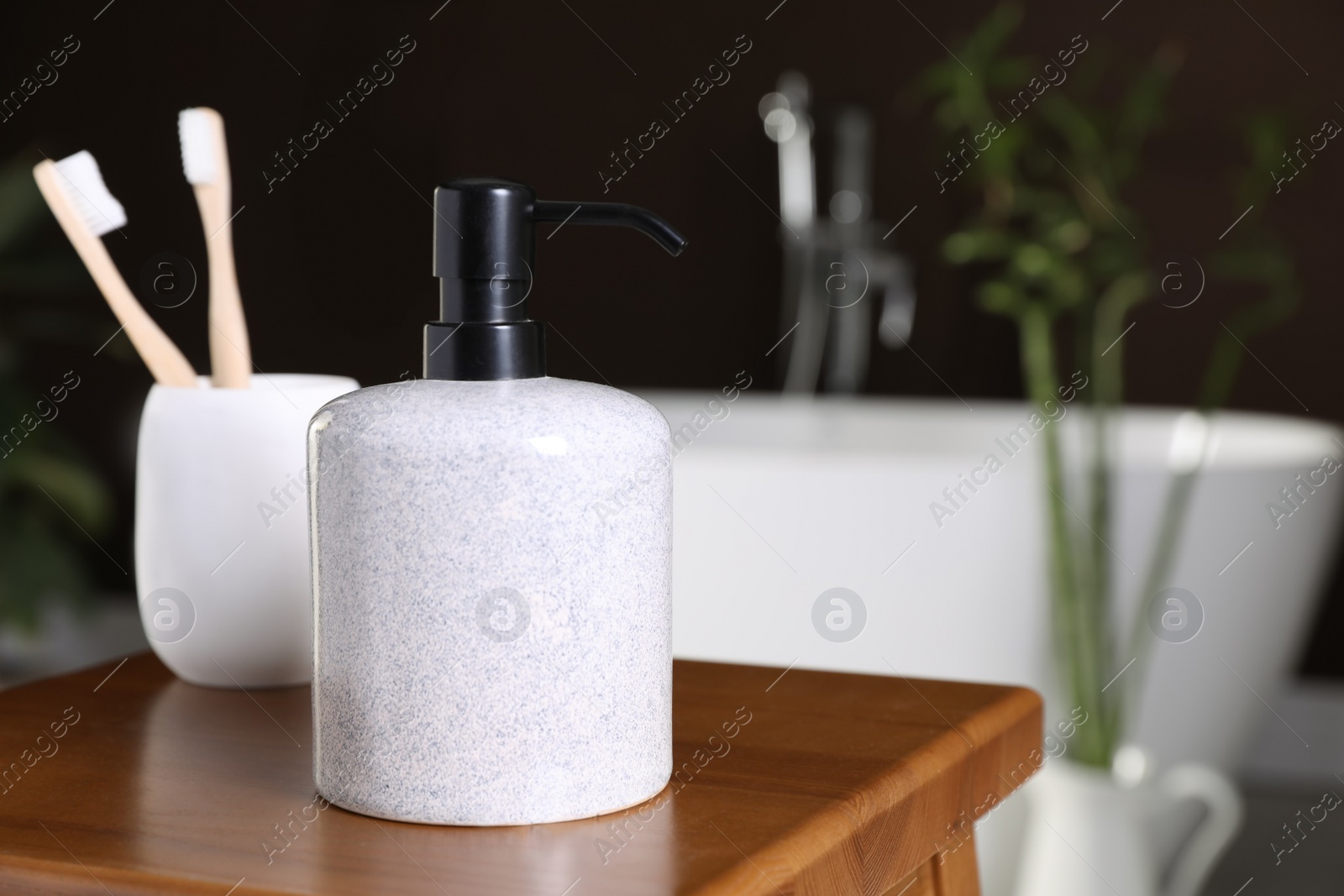 Photo of Dispenser of liquid soap and toothbrushes on wooden table in bathroom, space for text