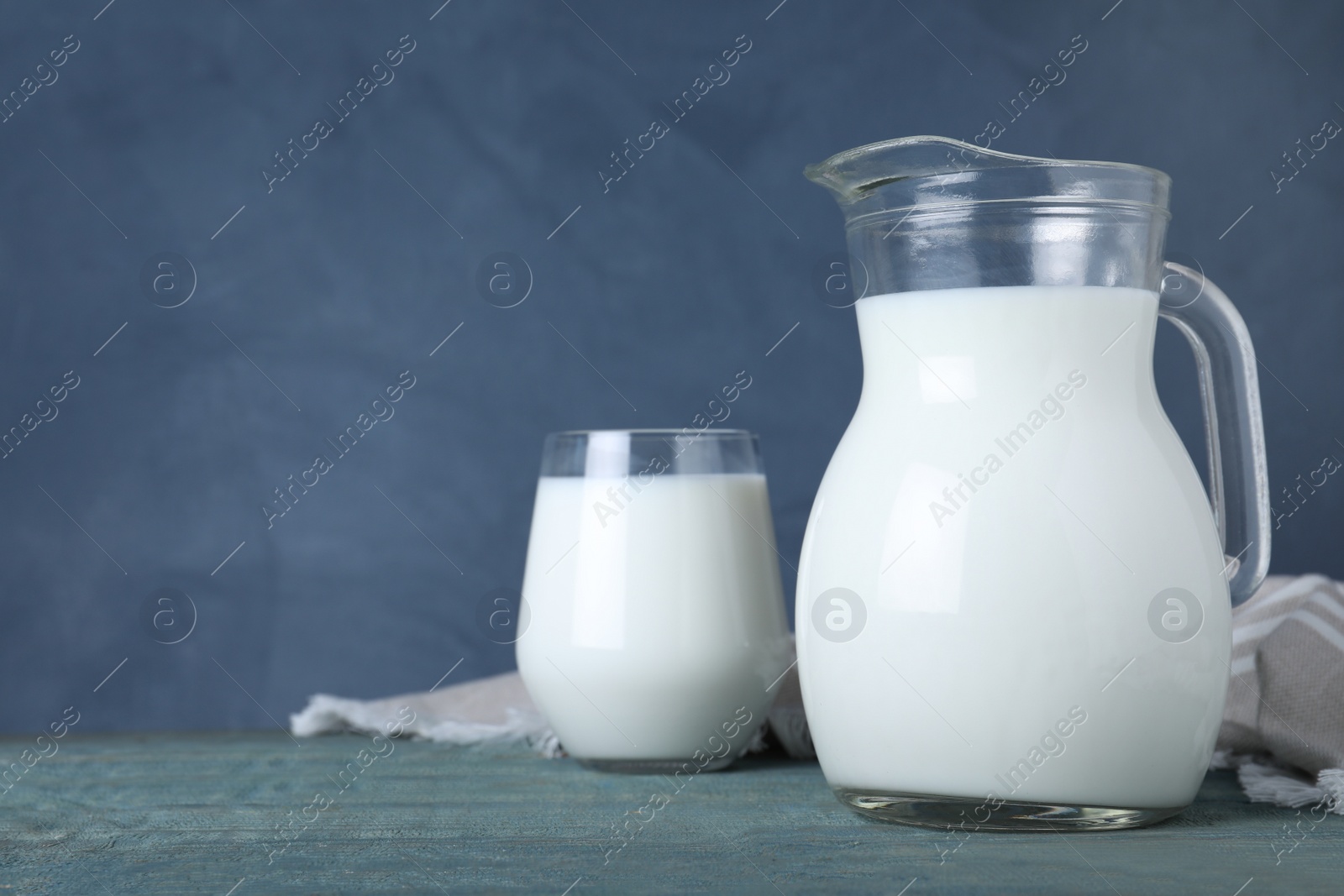 Photo of Jug and glass with fresh milk on wooden table against blue background. Space for text