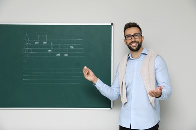 Photo of Teacher near green chalkboard with music notes in classroom