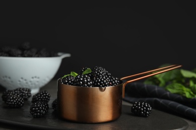 Metal saucepan with tasty blackberries on slate plate