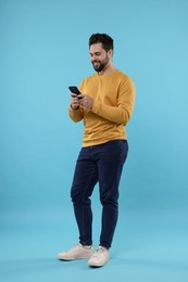 Photo of Happy young man using smartphone on light blue background