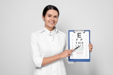 Ophthalmologist pointing at vision test chart on light background