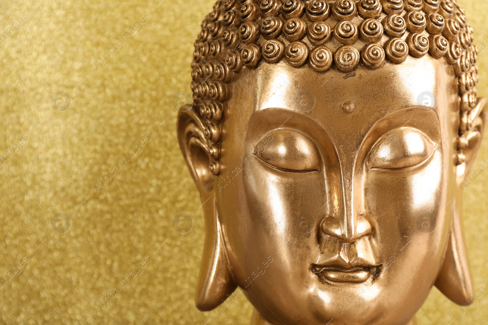 Photo of Buddha statue on golden background, closeup. Space for text