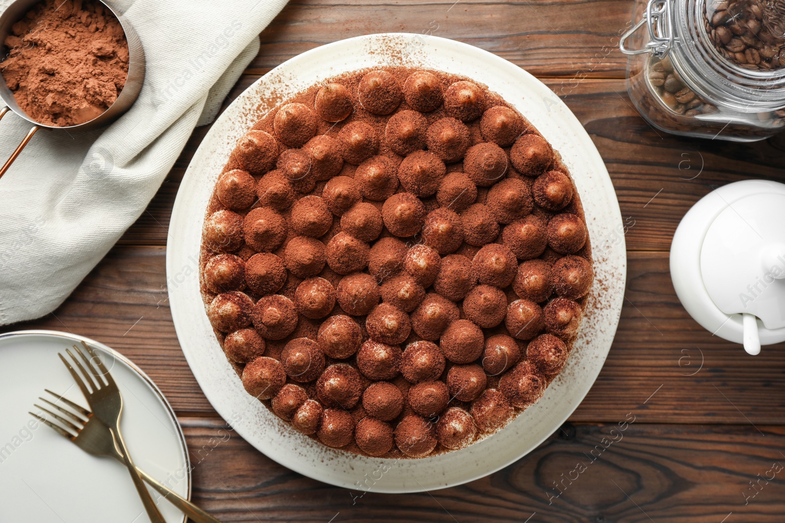 Photo of Delicious tiramisu cake with cocoa powder on wooden table, flat lay