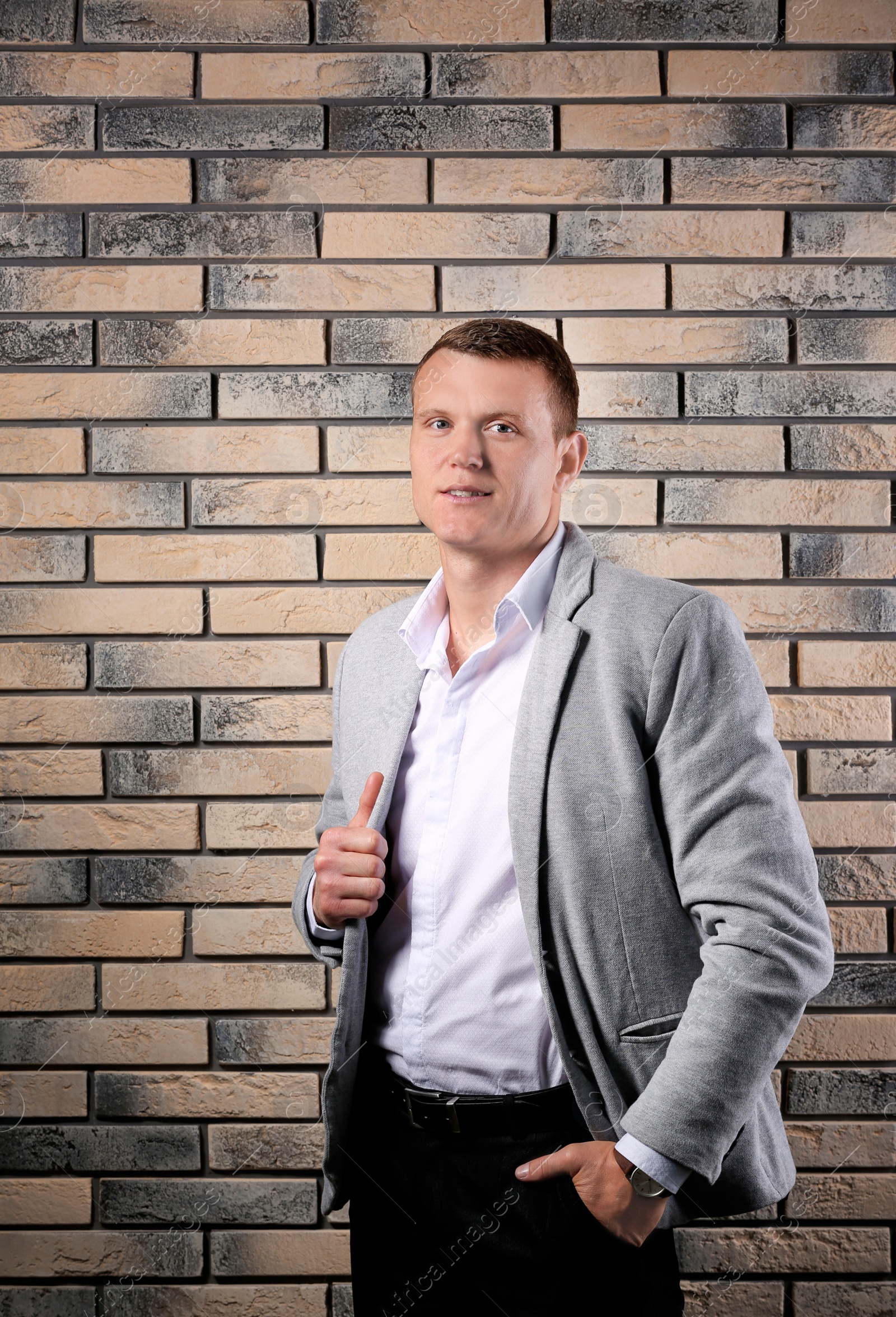 Photo of Handsome young man in suit near brick wall background